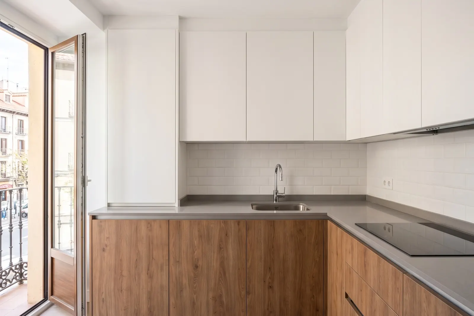 Cocina reformada con muebles blancos y madera junto a un balcón